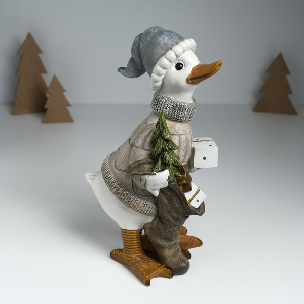 Изображение товара Статуэтка No Brand Гусь в бежевом свитере, с носком с подарками и елкой / 10325904