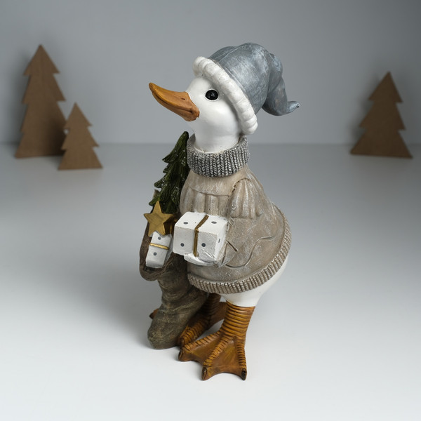 Изображение товара Статуэтка No Brand Гусь в бежевом свитере, с носком с подарками и елкой / 10325904